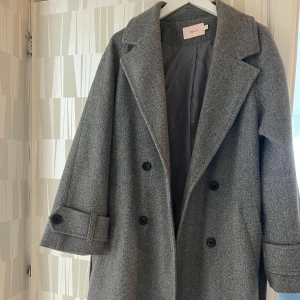Grå kappa från Nelly - Snygg grå kappa från Nelly i storlek S. Den har en klassisk design med dubbelknäppning och breda ärmar. 280 kr! 