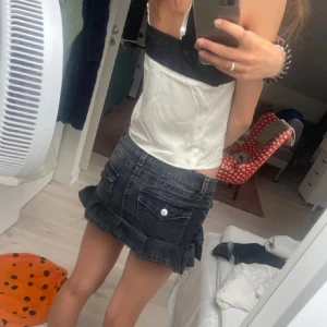 Svart jeanskjol med volanger - Trendig svart jeanskjol med flera lager av volanger. Kjolen har en klassisk jeansknäppning och fickor både fram och bak. Perfekt för en cool och avslappnad stil.