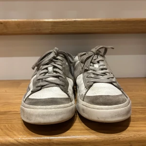 Vita och grå sneakers från Polo - Snygga sneakers från Polo i vitt och grått med den klassiska Polo-loggan på sidan. Skorna har snörning och en bekväm rund tå. Perfekta för en avslappnad stil. var håll i hällen men har lagats och läker inte in vatten i sulan 