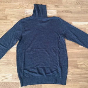 Mörkgrå polotröja - Säljer en stilren mörkgrå polotröja med långa ärmar. Tröjan är tillverkad i ett mjukt material och har ribbade muddar vid ärmslut och nederkant. Perfekt för kyligare dagar.