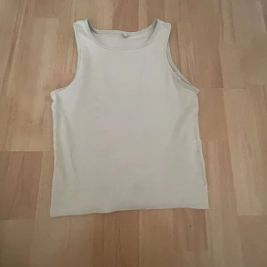 Beige ärmlös linnetopp - Säljer en stilren beige ärmlös linnetopp. Perfekt för varma dagar och enkel att matcha med olika outfits. Toppen har en klassisk rund halsringning och är tillverkad i ett mjukt material.