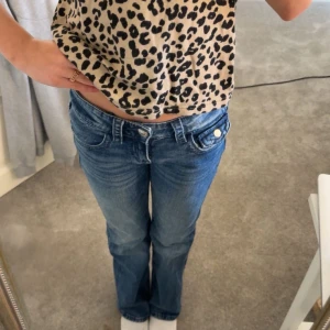 Blå jeans med broderade detaljer - Snygga blå jeans med broderade rosetter på bakfickorna. De har en klassisk femficksdesign och en bekväm passform. 