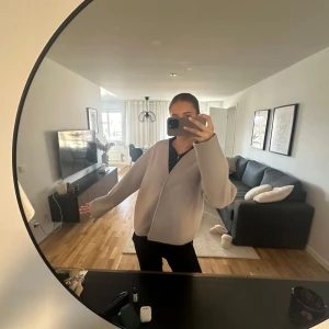 Beige kappa från Kappahl - Säljer en stilren beige kappa från Kappahl i storlek S. Jackan har en enkel design med knappar framtill och långa ärmar. Perfekt för en elegant look.