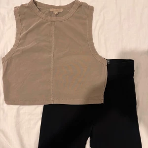 TVÅ FÖR 50:- Beige ärmlös croppad topp och leggings. - Säljer en stilren beige ärmlös croppad topp och svarta leggings. Perfekt för varma dagar Enkel design med rund halsringning. Topp, storlek S/M , leggings storlek XS/S