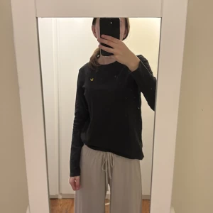 Svart långärmad tröja från Lyle & Scott - Säljer en svart långärmad tröja från Lyle & Scott med deras ikoniska gula logga på bröstet. Den är i storlek 12-13 år men jag som snart är 18 och bär storlek XS/S passar den fortfarande, både i armar, längden och är inte trång 