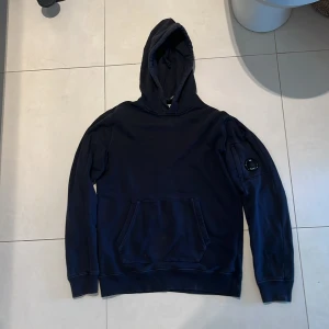 C.P Company - Säljer en snygg mörkblå hoodie från C.P. Company med en cool detalj på ärmen. Perfekt för en avslappnad stil. Självklart äkta. Tveka inte på att ställa nån fråga👋