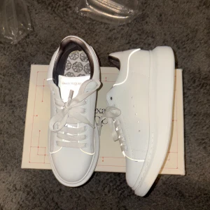  Alexander McQueen - Säljer ett par stilrena vita sneakers från Alexander McQueen. Skorna har en klassisk design med snörning och en tjock sula. Perfekta för en trendig och modern look.