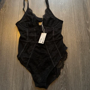 Svart spetsbody från NA-KD - Elegant svart body från NA-KD med spetsdetaljer och justerbara axelband. Perfekt för en stilfull look med en touch av lyx. Den har en jätte fin passform och passar perfekt till utgång eller fest🥰storlek 75A
