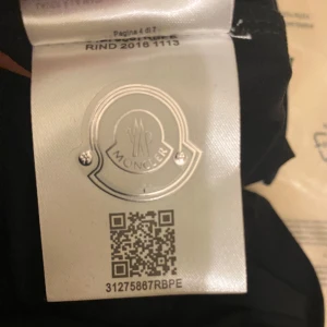 Svart Moncler pikétröja - Säljer en stilren svart pikétröja från Moncler med klassisk krage och röd-vita detaljer. Tröjan har Monclers logotyp på bröstet och är perfekt för en avslappnad men snygg look.