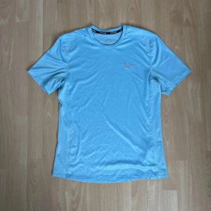 Ljusblå t-shirt från Nike - Säljer en ljusblå t-shirt från Nike med korta ärmar och rund hals. Perfekt för träning eller en avslappnad dag. Den har en liten Nike-logga på bröstet. Skön och lätt att bära!