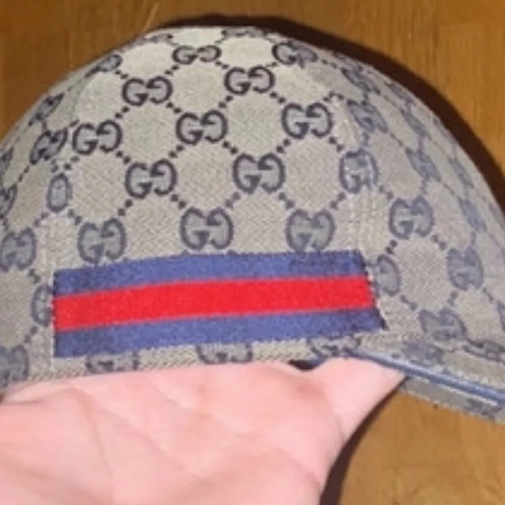 Säljer en stilren keps från Gucci med det ikoniska GG-mönstret i beige och blått. Kepsen har en röd och blå randdetalj på sidan. Perfekt för att ge din outfit en lyxig touch.. Asusteet.