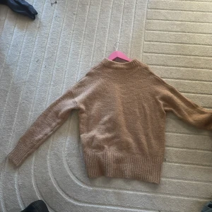 Beige stickad tröja - Mysig beige stickad tröja med långa ärmar och ribbade muddar. Perfekt för kyligare dagar.