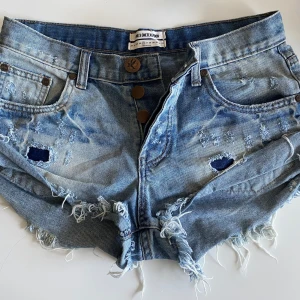 Jeansshorts från One Teaspoon stl 26  - Säljer ett par lågmidjade jeansshorts från One Teaspoon med slitna detaljer och fransar. Stl 26. Mätt rakt över 37 cm. Modell Bandits. Mkt fina! Ej använda mkt alls 💞