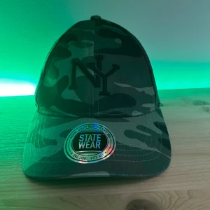 Camouflage keps från Statewear - Snygg keps i camouflage från Statewear med NY-broderi på framsidan. Perfekt för en avslappnad stil. Justerbar passform för att passa de flesta huvudstorlekar.