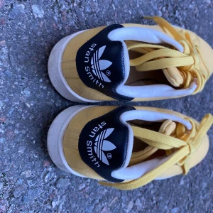 Gula Adidas Stan Smith sneakers - Säljer ett par gula Adidas Stan Smith sneakers med klassisk design och snörning. Skorna har en rund tå och vit sula med svart detalj på hälen. Perfekta för en färgglad touch till din outfit!pris kan diskuteras!