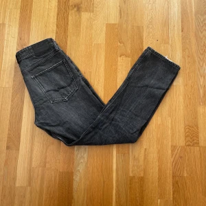 Svarta jeans från Jack & Jones - Snygga svarta jeansbyxor med en regular fit. De har en klassisk femficksdesign och en fransig detalj vid bensluten. Perfekta för en avslappnad stil. Lite slitna längst ned på benen.
