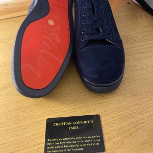 Blå sneakers från Christian Louboutin - Snygga blå sneakers från Christian Louboutin med den ikoniska röda sulan. Skorna har snörning och är tillverkade i ett lyxigt material som ger en exklusiv känsla. Perfekta för den som vill ha en stilren look med en touch av lyx.