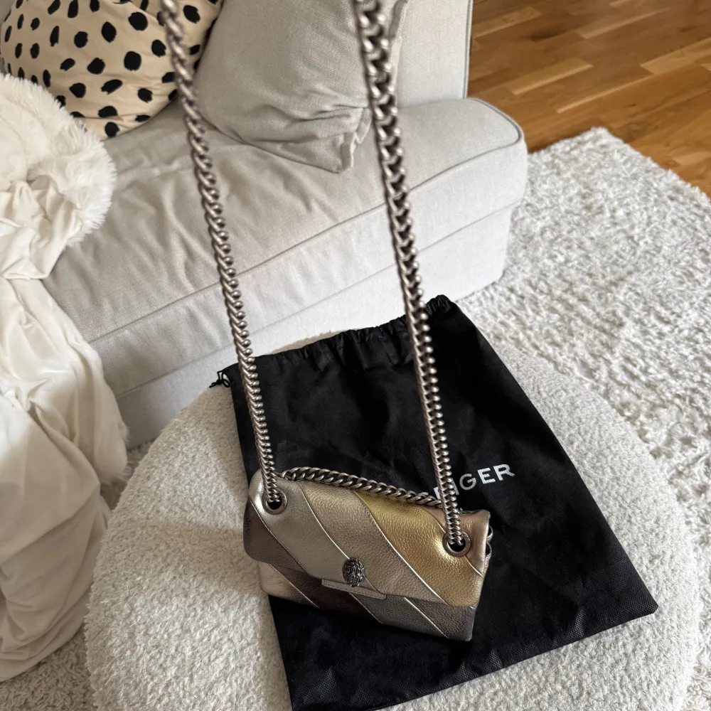 Snygg axelväska från Kurt Geiger i metalliska nyanser. Väskan har en kedjerem som går att justera så man kan bära både på axel samt crossbody. Säljer då den inte längre kommer till användning för jag köpt ny väska. . Laukut & Käsilaukut.