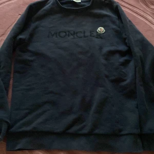 Mörk blå Moncler kofta  - Säljer en stilren svart tröja från Moncler med deras logotyp på bröstet. Tröjan har långa ärmar och en klassisk rund halsringning. Perfekt för en avslappnad men ändå elegant look. Pris kan diskuteras vid snabb affär 