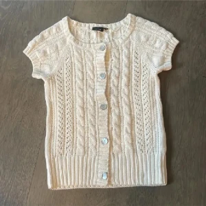 Vit stickad kofta med korta ärmar - Säljer en söt vit stickad kofta med korta ärmar och knappar framtill. Den har ett fint flätmönster och ribbade kanter som ger en klassisk look. Perfekt för lager-på-lager-stil! Otrolig fin nu till vår och sommar då den passar till allt❤️