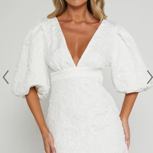 Showpo vit klänning med puffärmar - Elegant vit klänning med djup v-ringning och puffiga trekvartsärmar. Som är helt oanvänd med prislappen kvar. Passar perfekt till studenten! Köpt för 1250kr.