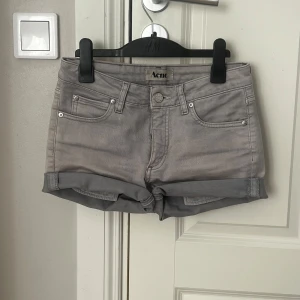 Grå lågmidjade jeansshorts från Acne - Snygga grå jeansshorts från Acne med klassisk femficksdesign och uppvikta benslut. De har en knappgylf och bälteshällor för extra stil och funktion. Lågmidjade snygga🫶🏼🎀 Äkta!