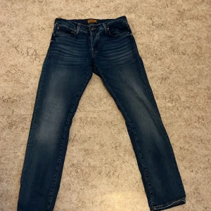 Blå jeans från Jack & Jones - Säljer ett par snygga blå jeans från Jack & Jones, modell Slim/Glenn. De har en slim passform och är tillverkade i ett klassiskt jeansmaterial. Perfekta för en stilren look.