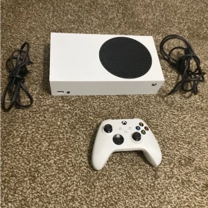 Xbox Series S 512 GB - Säljer en Xbox Series S med 512 GB SSD. Konsolen är vit med en svart cirkulär ventilationsöppning. Inkluderar en vit trådlös handkontroll och nödvändiga kablar. Perfekt för gaming med hög prestanda i ett kompakt format.