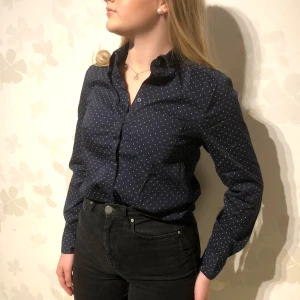 Mörkblå prickig skjorta - Snygg mörkblå skjorta med små vita prickar. Skjortan har långa ärmar och en klassisk krage. Perfekt för en stilren look.