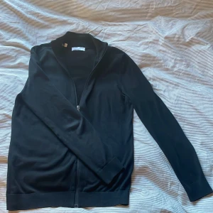 Svart full zip - Säljer en stilren svart stickad tröja från Selected Homme. Tröjan har en dragkedja framtill och långa ärmar. Perfekt för en avslappnad och snygg look. Mycket bra skick, skriv vid minsta fundering!