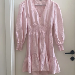Rosa klänning från Zara - Söt rosa klänning från Zara med v-ringning och långa ärmar. Klänningen har en smockdetalj i midjan och volanger vid fållen. Perfekt som skolavslutningsklänning 