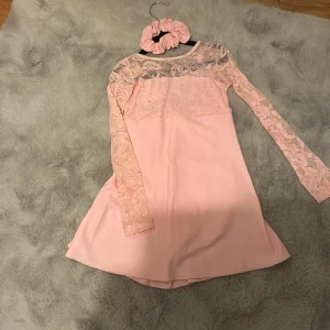 Rosa konståkningsklänning med spetsdetaljer - Vacker och stilren lyckradräkt från Sagester med stretchig spets upptill som går över i långa ärmar. AB Swarovskikristaller är utspridda över dräkten. Rosett i band som går att knyta såväl fram som bak. Håraccesoar medföljer. 6-7 år ca 24-31kg nypris 1699kr 