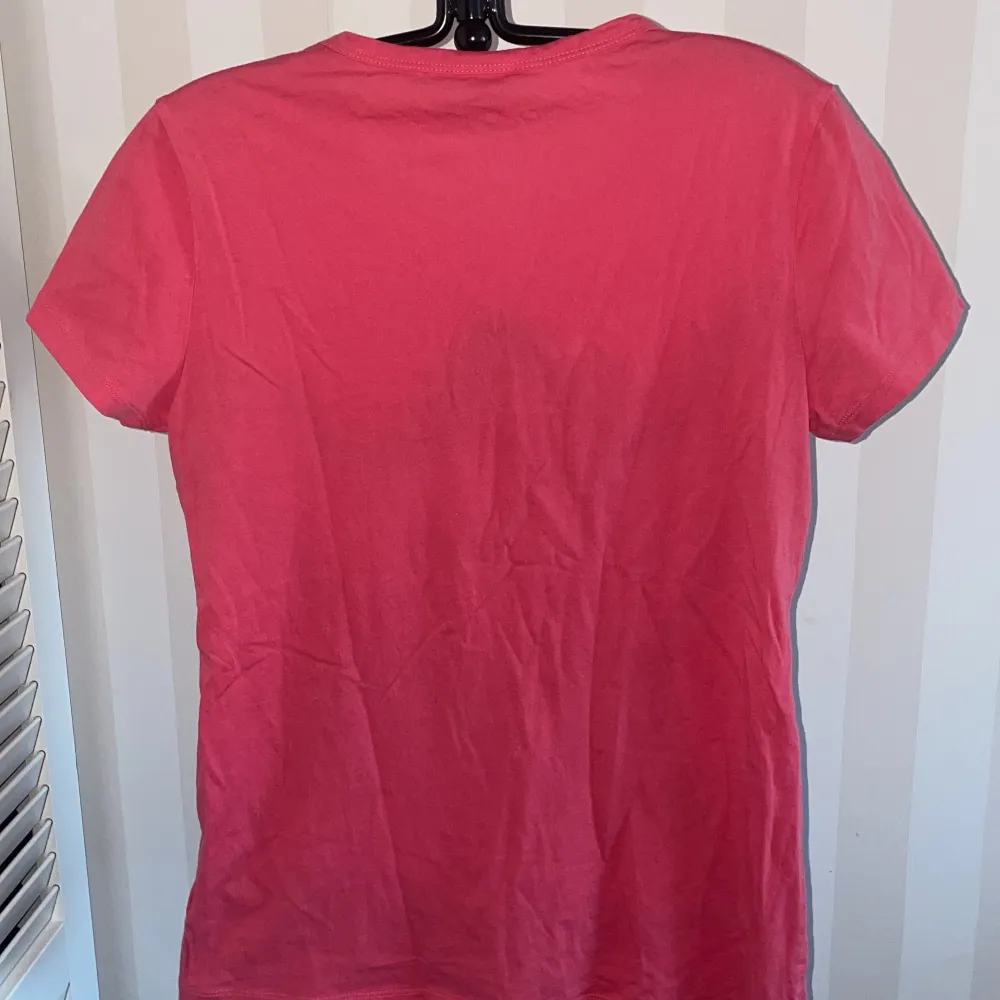 Snygg rosa t-shirt från DKNY med ett coolt tryck av en kvinna på framsidan. Perfekt för en avslappnad stil med en touch av attityd. Kortärmad och tillverkad i mjukt material för extra komfort.. T-paidat.