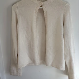 Beige stickad kofta - Säljer en stilren beige stickad kofta med långärmad design. Koftan har en enkel knappdetalj vid halsen och är perfekt för lager-på-lager-stil. Passar bra till både vardag och mer uppklädda tillfällen.🩷