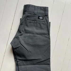 Grå byxor från Dickies - Snygga grå byxor från Dickies med slim passform. Perfekta för en stilren look. Byxorna har en klassisk design med fickor och bälteshällor. W28 L30