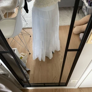 Vit långkjol från New Collection - Säljer en vacker vit långkjol från New Collection. Kjolen har en luftig och flödande design med flera lager som ger en fin volym. Perfekt för sommarens varma dagar. Resår i midjan för en bekväm passform. Endast använd en gång