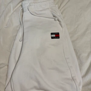 Vita mjukisbyxor från Tommy Jeans - Snygga vita mjukisbyxor från Tommy Jeans med broderad logga på benet. Byxorna har resår och snörning i midjan för skön passform. Perfekta för chill dagar eller när du vill ha en clean och stilren look.