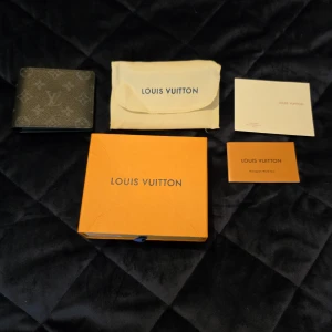 Louis Vuitton svart plånbok i skinn - Säljer en snygg svart plånbok från Louis Vuitton med klassiskt monogrammönster. Plånboken är tillverkad i textil med insida i kalvskinn och har flera kortfack. Kommer med original ask, dustbag och äkthetskort. Perfekt för dig som vill ha något stilrent och lyxigt i fickan.