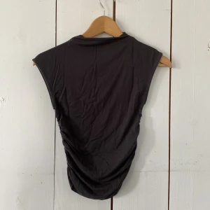 Svart ärmlös topp från Gina Tricot - Snygg svart ärmlös topp från Gina Tricot i storlek XS. Toppen har cool rynkade sidor som ger en unik look och är gjord i mjuk bomull. Perfekt att styla med jeans eller kjol för en trendig vibe.