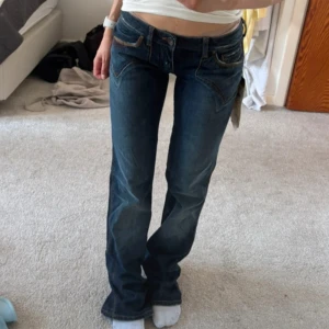 Blå Rodeo jeans med broderade fickor - Säljer ett par blå jeans från Rodeo med snygga broderade detaljer på bakfickorna och kontrastsömmar. Modellen är lågmidjad med raka ben och klassisk femficksdesign. Jeansen har en cool western-vibe och är gjorda i bomullsdenim. Midjemått: 39 Innebärslängd: 83