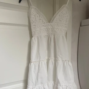 Vit spetsklänning med volanger - Superfin vit klänning med spets upptill, smala axelband och volanger i kjolen. Djup v-ringning och öppen rygg med knytband ❤️Storlek M. Finns även på min vinted: mariabeckman