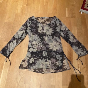 Blommig blus - En semi genomskinlig blus från Vila med fint blom mönster och en liten knapp framtill, den äe justerbar i midjan och längst ut på ärmarna(ärmarna går typ lite förbi armbågarna) mycket bra skick!