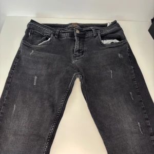 Svarta jeans från BOSS med slitningar - Snygga svarta jeans från BOSS med diskreta slitningar och coola detaljer. Jeansen har klassisk femficksmodell, silverfärgad knapp och dragkedja samt unikt mönstrat innerfoder. Perfekta för dig som gillar en avslappnad men stilren look.              Passer S och M, använda 2-3 gånger, nytvättade 