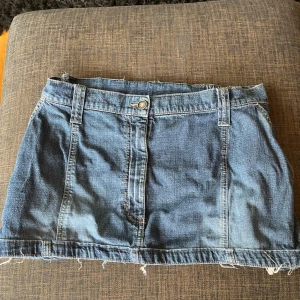Blå jeanskjol med rå kant - Säljer en super fin lågmidjad blå jeanskjol med fransig kant nertill. Kjolen är i en kort modell. Pris kan diskuteras vid snabb affär.