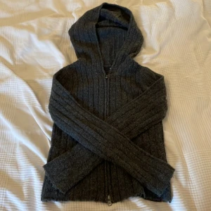 Mörkgrå stickad hoodie från 157 XS - Mysig mörkgrå stickad hoodie från 157 i storlek XS. Tröjan har huva, dragkedja framtill och ribbad struktur. Perfekt för kalla dagar när du vill vara både bekväm och snygg.