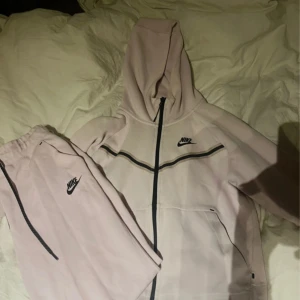 Ljusrosa mjukisbyxor från Nike XS - Säljer ett par ljusrosa mjukisbyxor och tröja från Nike i storlek XS. Byxorna har svarta dragsnören i midjan, elastisk midja och en svart Nike-logga på benet. Perfekta för chill eller träning, riktigt sköna och snygga. Passar även storlek s