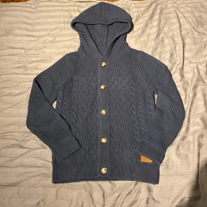 Mörkblå stickad hoodie-kofta Pier One - Snygg kofta med luva från pier one. Ribbstickad med en brytning av kabelstickat över mage och bröst. Försluten med knappar i havannastil. Använd endast två gånger och tvättad en gång. Säljer då den är för stor för mig.                                                          //Hugo