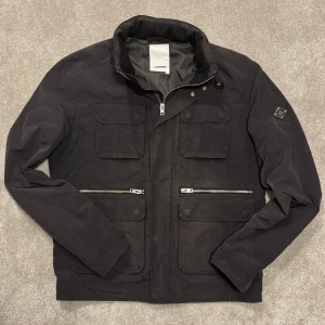J.Lindeberg fieldjacket - Tja! Säljer denna feta svarta fieldjackan från J.Lindeberg! Jackan är i gott skick och har den eftertraktade silvriga badgen på armen! Size L men passar M, modellen på bilden är 182cm lång ish. Skriv vid funderingar!