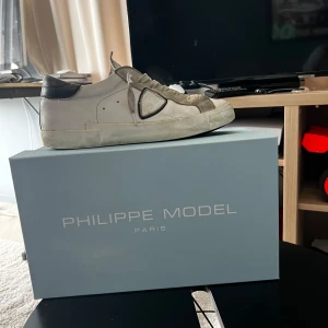 Philippe Model vita sneakers i skinn - Snygga vita sneakers från Philippe Model Paris med grå och svarta detaljer. Skorna har klassisk låg profil, slitningar snörning och rund tå. Ovandelen är i skinn med mockadetaljer och svart hälparti. Perfekta för en clean och stilren look.                             Pris kan diskuteras 