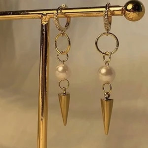 Guldiga örhängen med pärlor och spikes - Snygga örhängen i guldton med runda ringar, vita pärlor och coola konformade spikes. Perfekt accessoar för dig som vill sticka ut och addera lite edge till din stil. Passar både till streetwear och mer dressade outfits.